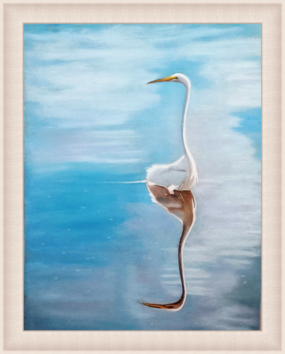 A framed painting of a white heron standing in calm blue water, with its reflection visible below. The artwork is presented in a light natural wood frame against a white background.