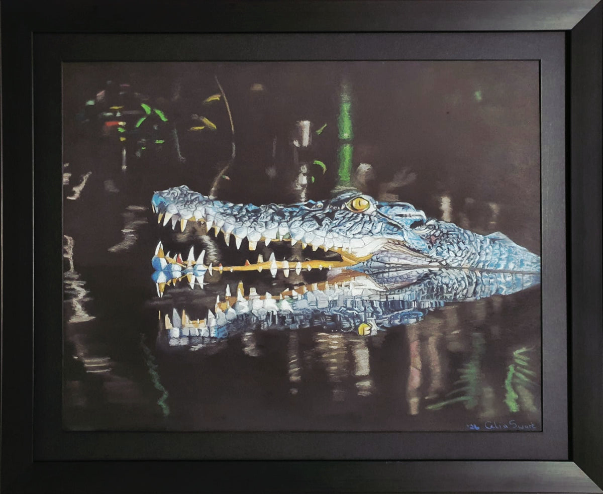 A framed painting of a blue and white alligator or crocodile with its mouth open, reflected in dark water. The artwork is presented in a black frame against a white background.