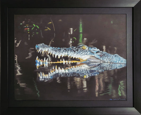 A framed painting of a blue and white alligator or crocodile with its mouth open, reflected in dark water. The artwork is presented in a black frame against a white background.
