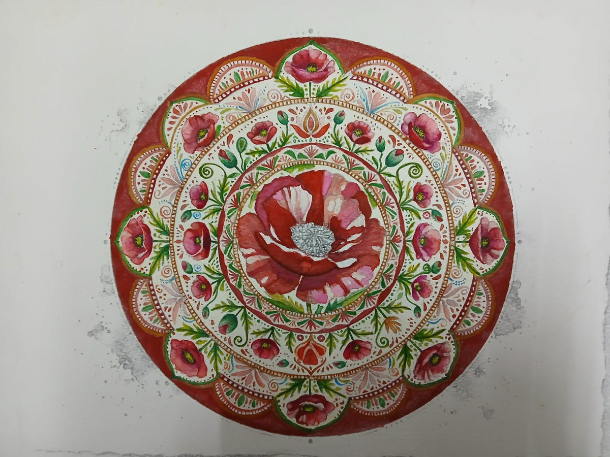 A round decorative plate or tray featuring an intricate hand-painted floral mandala design in red, pink, green, and white, set against a plain off-white background.